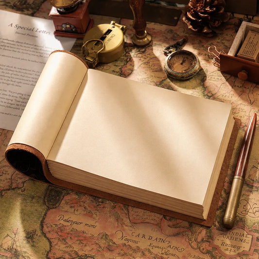 Open landscape leather journal with blank cream pages on a vintage map beside a wooden pen and antique watch.