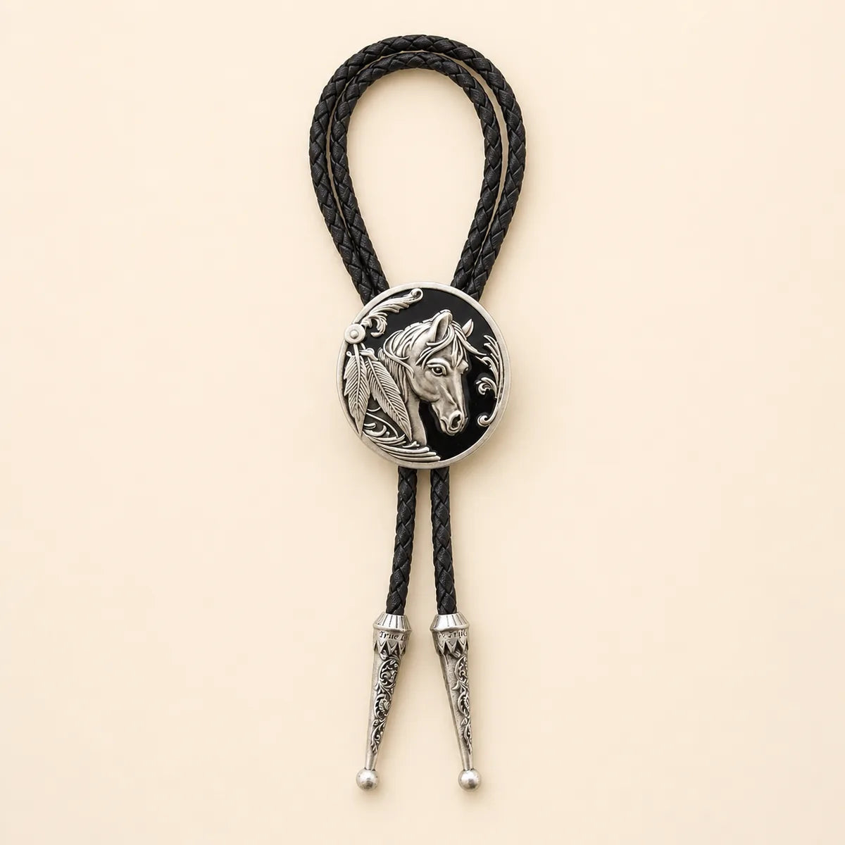 Black horse head bolo tie with antique silver medallion and braided leather cord on warm ivory background
