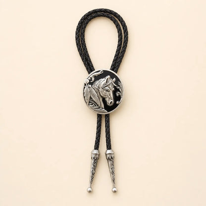 Black horse head bolo tie with antique silver medallion and braided leather cord on warm ivory background