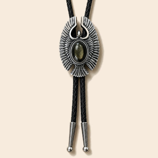 Eagle Wing golden obsidian bolo tie with antique silver-tone eagle frame and black braided cord on a warm ivory background