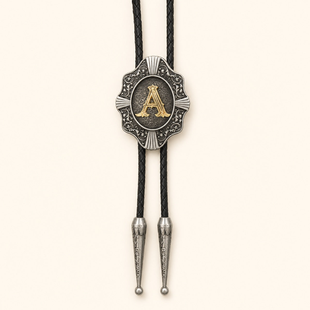 Gold letter A Western bolo tie with ornate antique silver medallion and black braided leather cord on warm ivory background