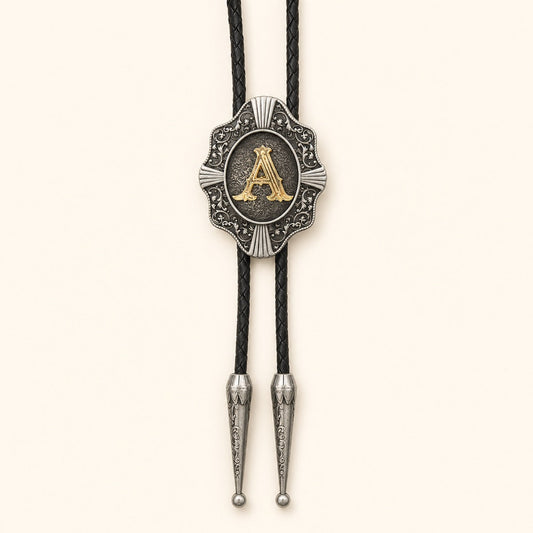 Gold letter A Western bolo tie with ornate antique silver medallion and black braided leather cord on warm ivory background