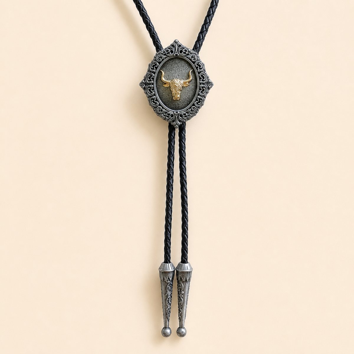 Gold longhorn bolo tie with antique silver scrollwork and braided leather cord on warm ivory background