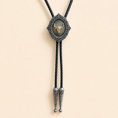 Gold longhorn bolo tie with antique silver scrollwork and braided leather cord on warm ivory background