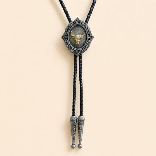 Gold longhorn bolo tie with antique silver scrollwork and braided leather cord on warm ivory background