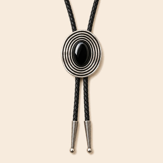 Orbit black obsidian bolo tie with antique silver-tone orbit frame and braided cowhide cord on a warm ivory background