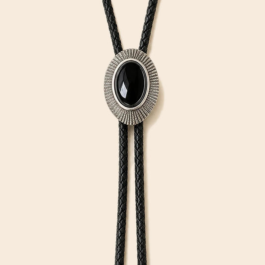Solstice black obsidian bolo tie with antique silver-tone frame and black cowhide cord on a warm ivory background