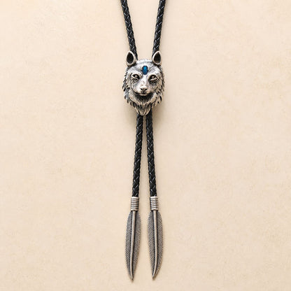 Stainless steel blue inlay wolf head bolo tie with black braided leather cord and feather-shaped tips on a warm ivory background