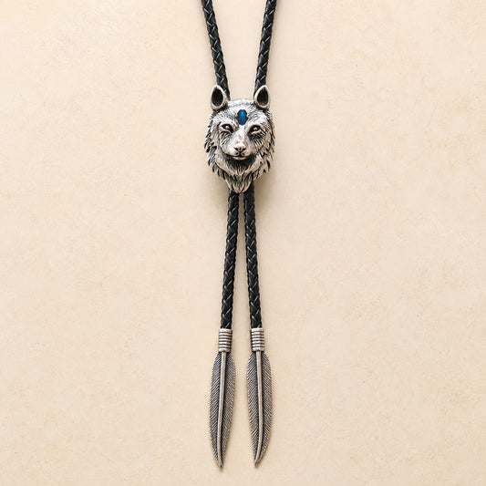 Stainless steel blue inlay wolf head bolo tie with black braided leather cord and feather-shaped tips on a warm ivory background