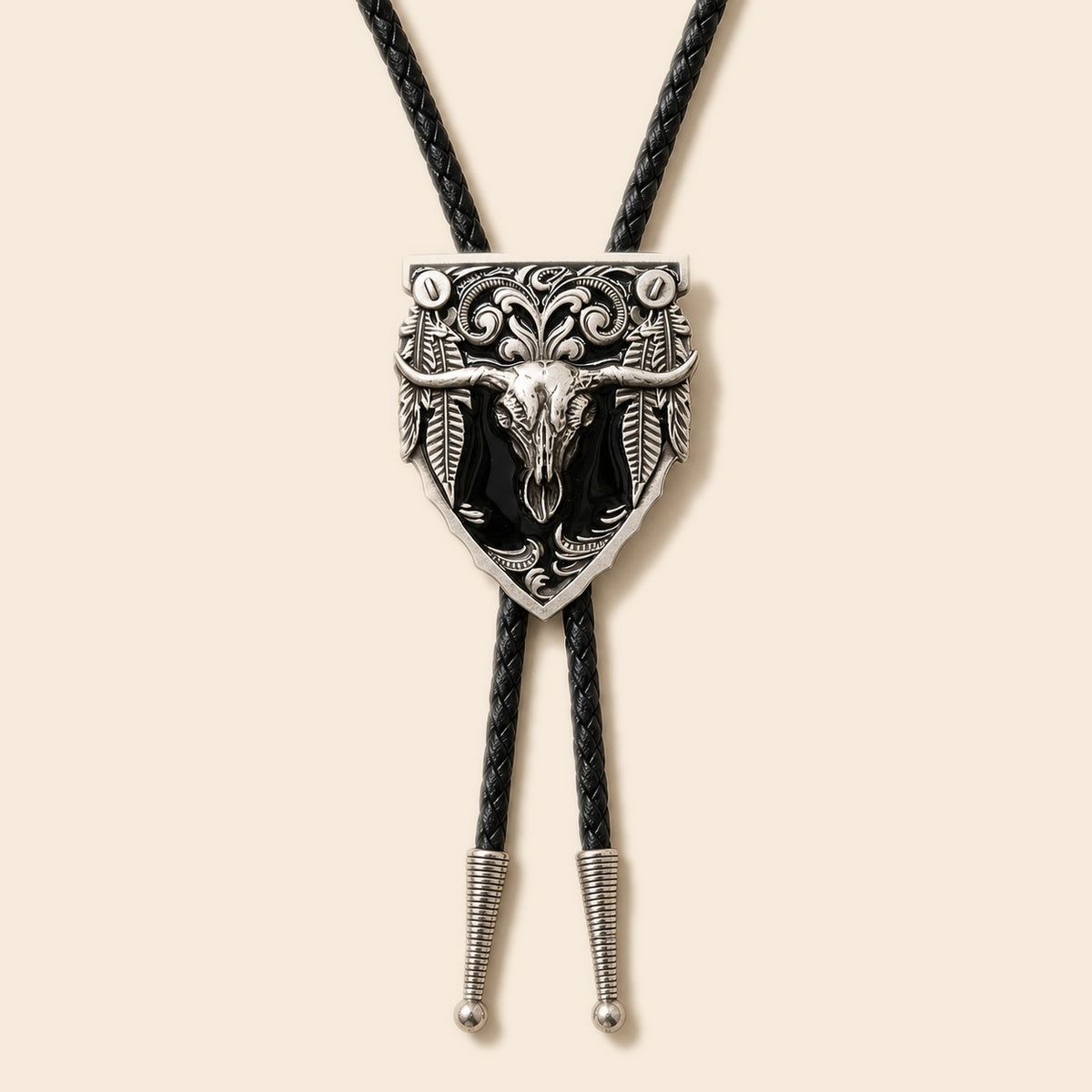 Western black longhorn skull cold enamel bolo tie with silver-tone shield medallion and braided leather cord on a warm ivory background