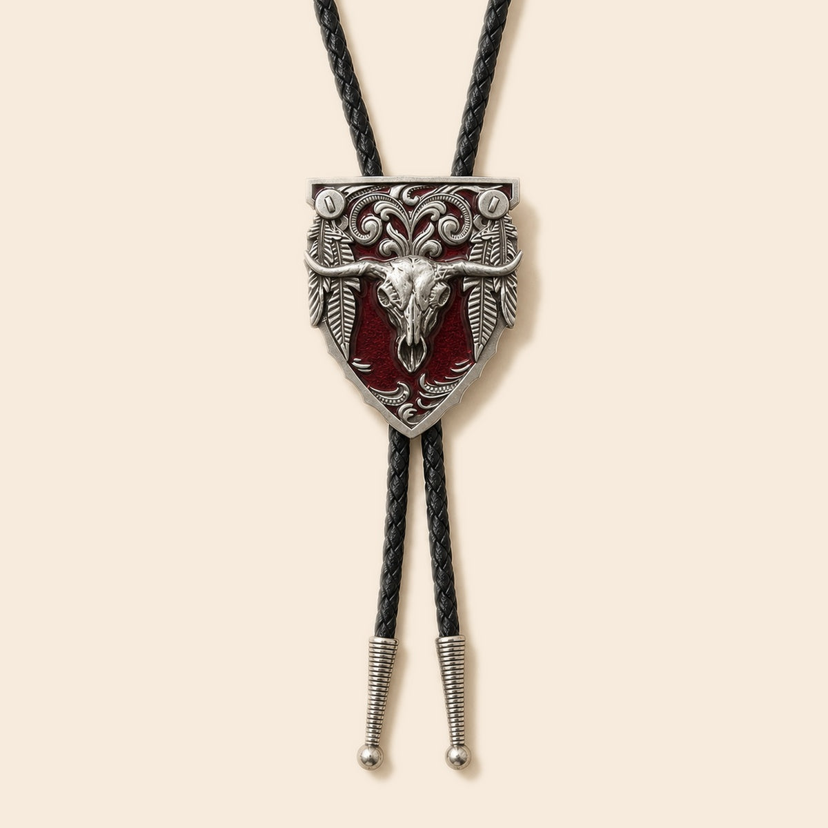 Western red longhorn skull cold enamel bolo tie with silver-tone shield medallion and braided leather cord on a warm ivory background