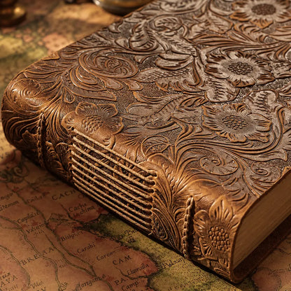 Close-up of the brown floral cowhide cover and exposed cord stitching on the short spine of a landscape journal.