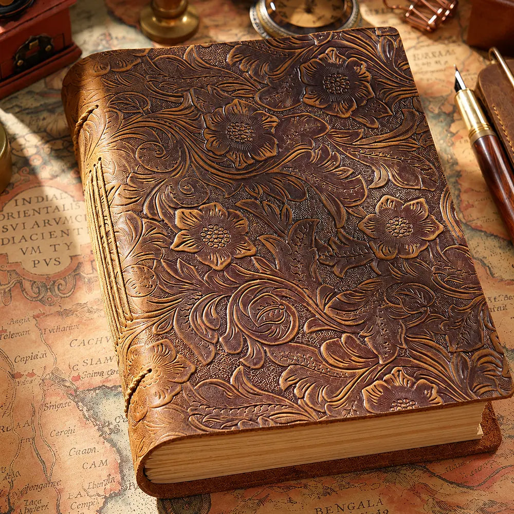Close-up of floral and scrolling leaf details on the brown cowhide journal cover and stitched spine.