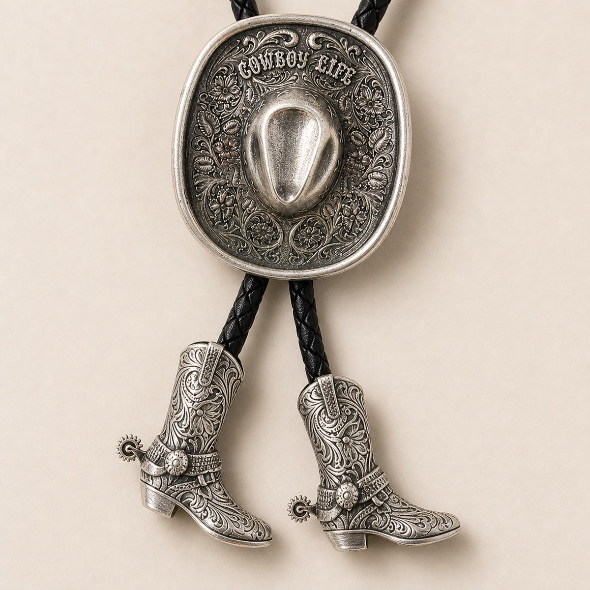 Close-up detail of silver Cowboy Life hat bolo tie with floral tooling and cowboy boot pendants