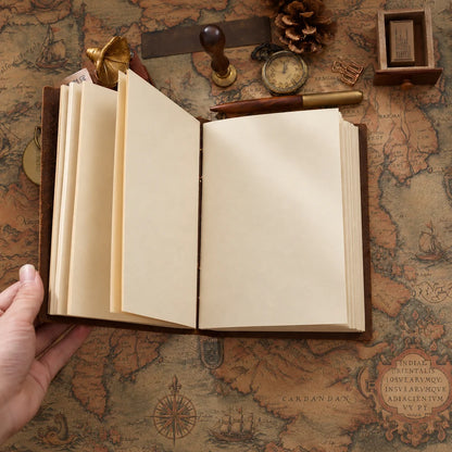 Open brown leather journal with blank cream pages and visible center stitching on a vintage map.