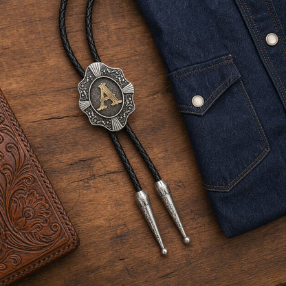 Gold letter A Western bolo tie arranged with dark denim and tooled leather on walnut wood
