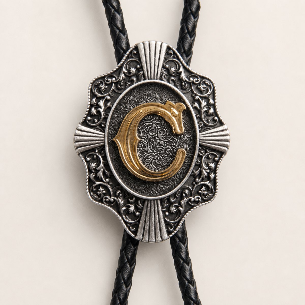 Close-up of gold initial C and engraved antique silver bolo tie craftsmanship