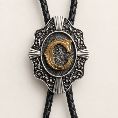 Close-up of gold initial C and engraved antique silver bolo tie craftsmanship