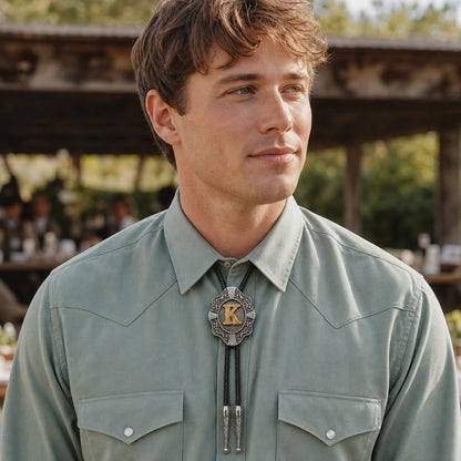Young man wearing gold letter K Western bolo tie at a ranch wedding