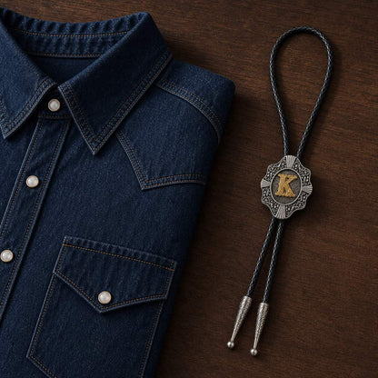 Gold letter K Western bolo tie beside denim shirt on walnut