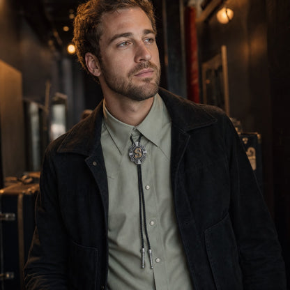 Young man wearing gold letter S bolo tie backstage at a music venue