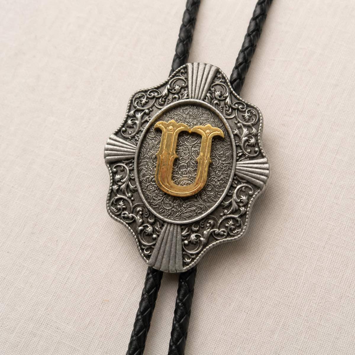 Gold letter U bolo tie antique silver engraving and leather detail