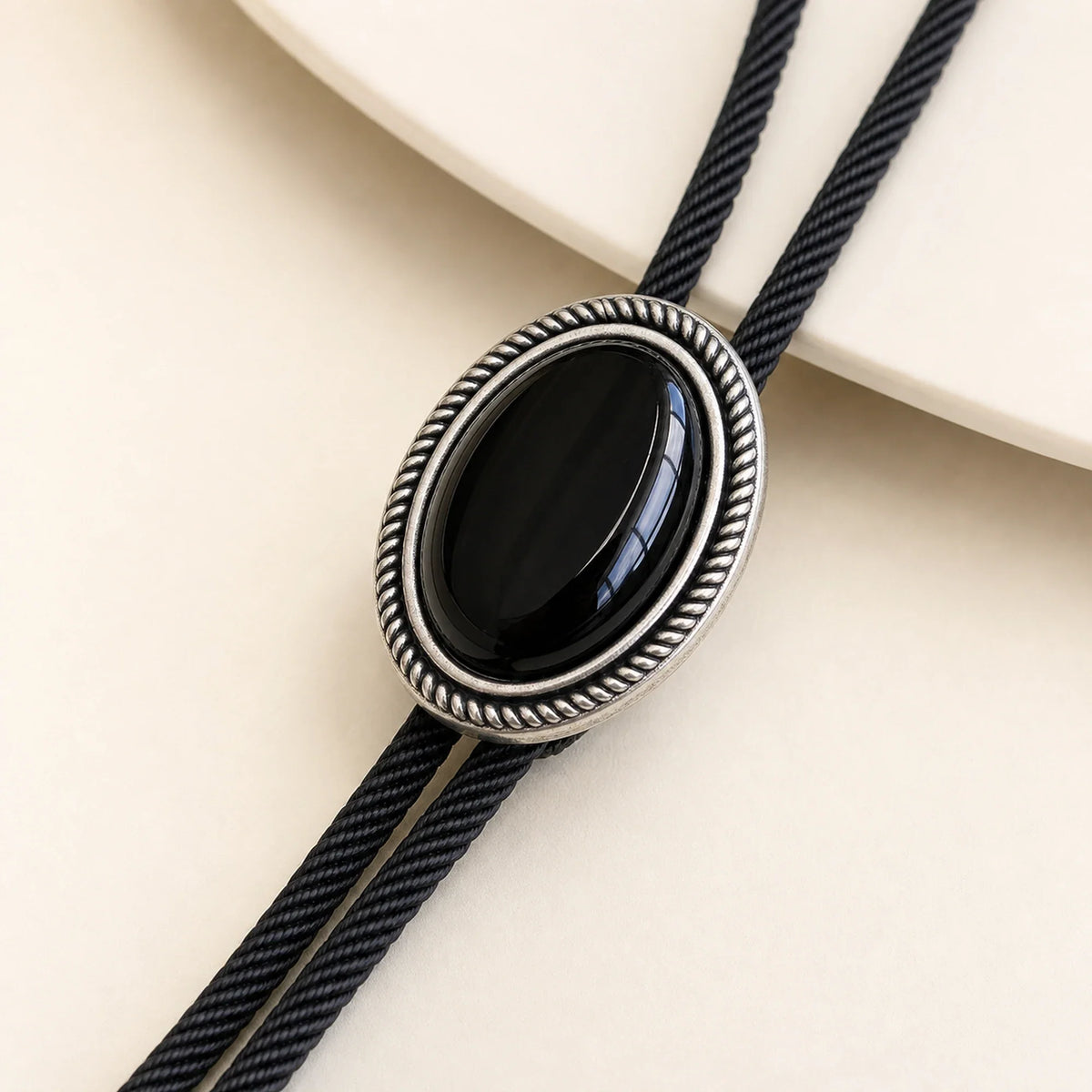 Close-up detail of natural black obsidian stone and antique silver-tone rope-border bolo tie frame
